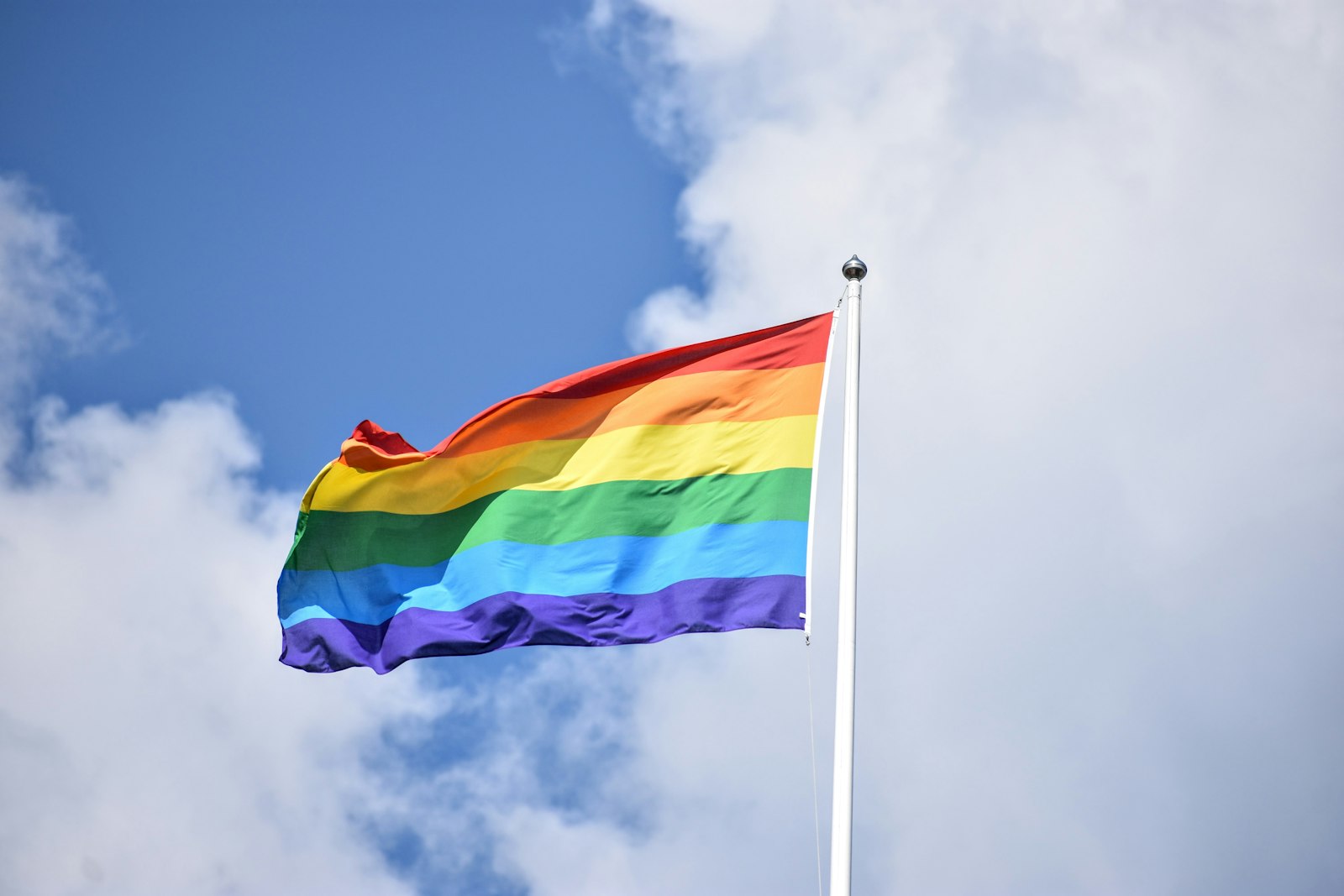 A rainbow Pride flag lifting in the wind against a bright blue sky