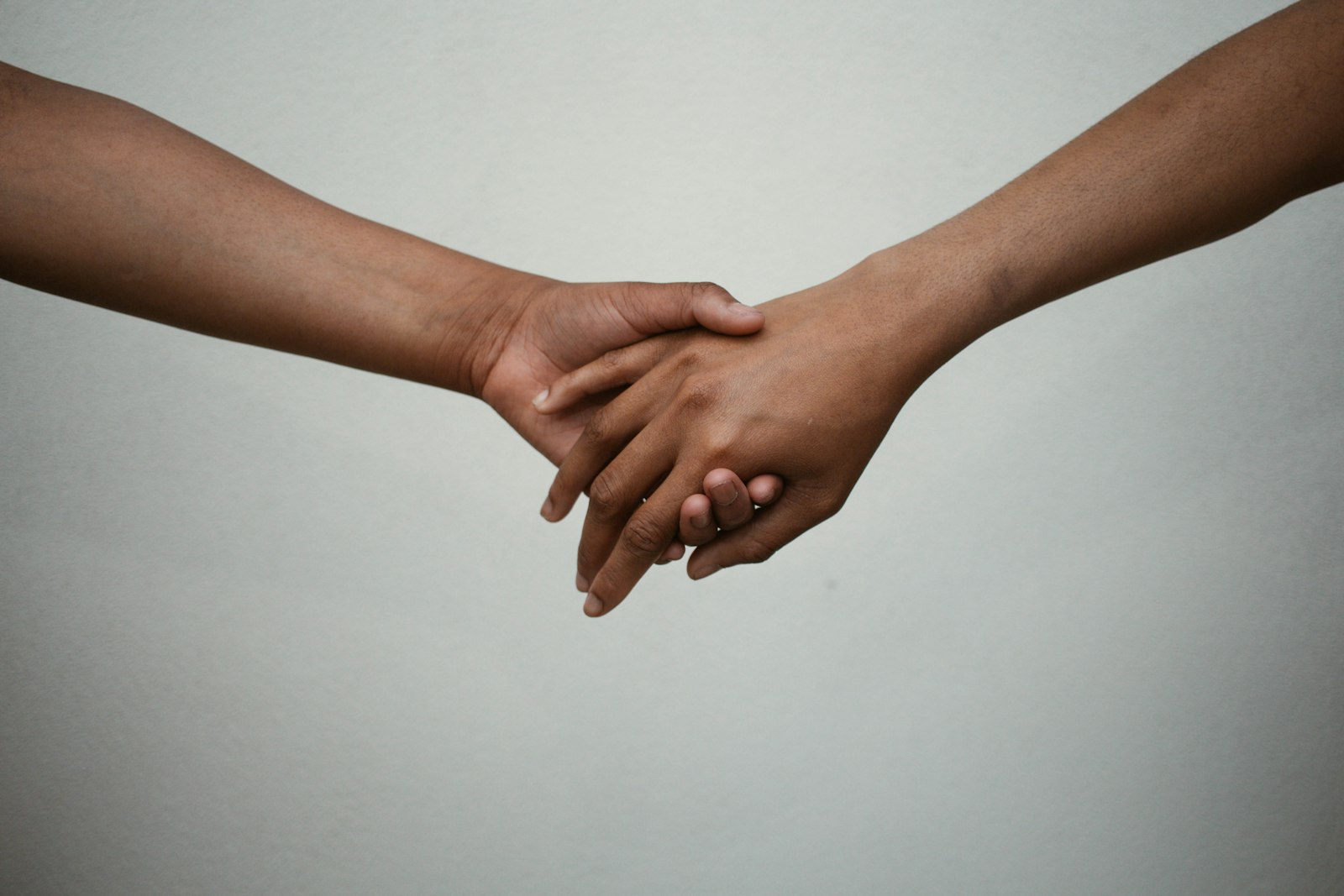 Two people reaching toward each other and clasping hands against a soft neutral background